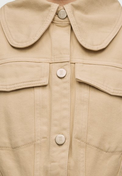 Μπεζ ζακέτα με κουμπιά, φαρδιά γιακά, δύο τσέπες στο στήθος με καπάκια και ανάγλυφα στρογγυλά μεταλλικά κουμπιά στο μπροστινό μέρος.
