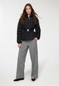 Czarna puchowa kurtka z paskiem w talii, prążkowanym kołnierzem i zapięciem na zamek. W zestawie z szerokimi spodniami w szaro-czarne kratę i czarnymi balerinami.