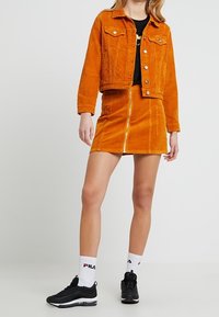 Röd kordjacka med två framfickor, matchad med en röd dragkedjeskjorta. Svarta sneakers och vita ankelstrumpor fulländar outfiten.