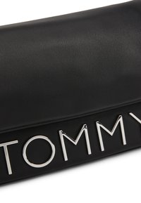 Bolso de mano negro texturizado con un logo plateado "TOMMY". El diseño es elegante, con una forma rectangular y superficie lisa.