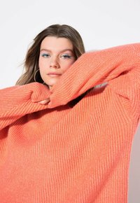 Maglione corallo dal taglio morbido con texture a coste e maniche lunghe, caratterizzato da una silhouette oversize e materiale a maglia morbido.