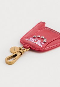 Portachiavi in pelle rossa con un gancio dorato, caratterizzato da strass decorativi in motivi floreali e un ciondolo con marchio.