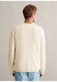 Cremfarbener Pullover aus strukturiertem Stoff, mit geripptem Hals- und Saumabschluss sowie langen Ärmeln. Die Rückansicht zeigt ein einfaches, minimalistisches Design.