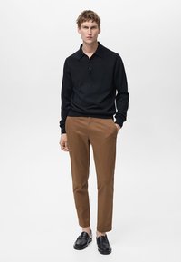 Čierna polokošeľa s dlhým rukávom a golierom, v kombinácii s hnedými slim-fit chinos a čiernymi mokasínmi. Jednoduchý a moderný dizajn.