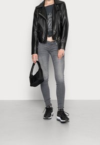 Chaqueta de cuero negra, camiseta gráfica gris, jeans ajustados grises y zapatillas negras. Sosteniendo un pequeño bolso negro.