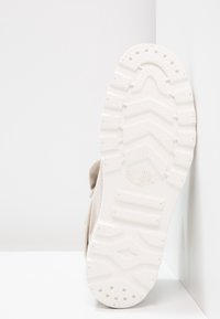 Sneaker beige chiaro con una parte superiore in tessuto testurizzato e una suola in gomma bianca spessa con un motivo a zig-zag e il logo del marchio.
