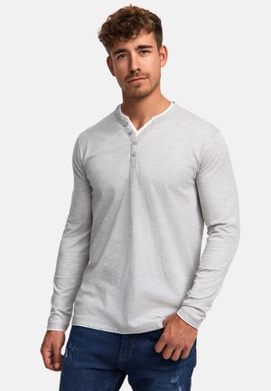 Camisa henley de manga larga gris con cuello redondo, tapeta de tres botones y una textura suave, combinada con jeans azules desgastados.