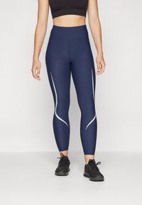 Marinehøy midje leggings laget av elastisk stoff, med lysegrå buede sidelister og en glatt tekstur, sammen med svarte joggesko.