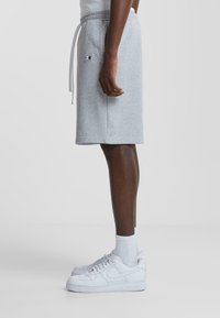 Shorts en coton gris avec une taille élastique et un cordon de serrage, arborant un petit logo. Associés à des baskets blanches et des chaussettes.