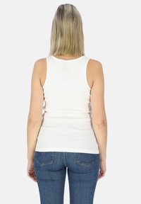 Witte geribbelde tanktop met een ronde hals, aangesloten ontwerp en rauwe zoom, gecombineerd met blauwe jeans in een klassieke vijf-pocketstijl.