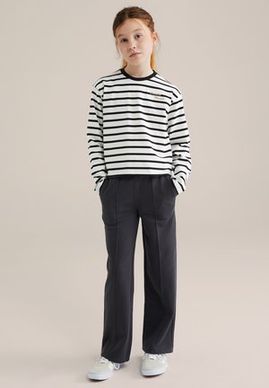 Camisa de manga larga a rayas en blanco y negro con cuello redondo, combinada con pantalones de pierna ancha en azul marino y zapatillas blancas.