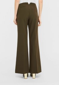 Pantaloni a gamba larga marroni realizzati in tessuto liscio, con vita alta e due tasche posteriori. L'orlo cade appena sopra le scarpe.