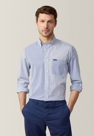 Blau-weißer gestreifter Hemd mit Kragen, einer Brusttasche, krempelbaren Ärmeln und einer glatten Baumwolltextur, kombiniert mit navyfarbenen Hosen.