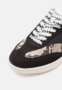 Baskets noires avec tige en daim, accents à motif serpent, lacets blancs et semelle en caoutchouc texturée. Présente un design à bout arrondi.