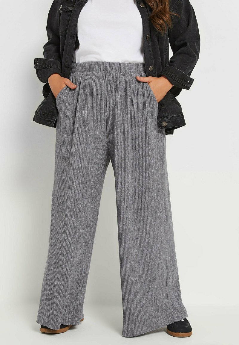 Grå, vida byxor med vertikal ribbad textur, elastisk midja och sidofickor, kombinerat med en svart jacka och vit topp.