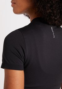 Černé sportovní tričko s krátkými rukávy a přiléhavým střihem. Na zádech je minimalistické logo a hladká, elastická textilie.