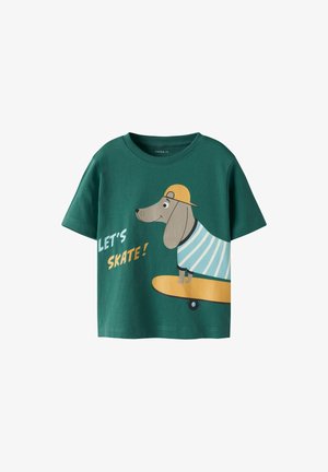 Camiseta de algodón verde con un diseño de manga corta. Presenta un gráfico de un perro en una patineta que lleva puesta una camisa a rayas y una gorra amarilla.