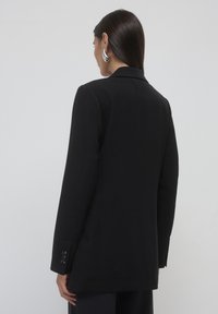 Black tailored blazer, single-breasted design, smooth texture, wide lapels, buttoned cuffs, and clean lines with a slightly elongated shape.