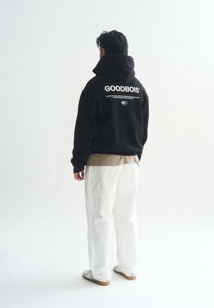 Black hoodie with white "GOODBOIS" text on the back, paired with light-colored pants. The fabric is soft and casual in style.