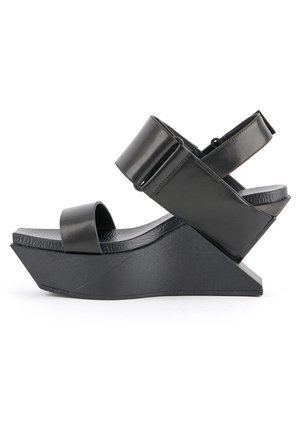 Sandale compensée noire avec une large bride avant, une bride de cheville épaisse avec boucle et un maintien slingback, dotée d'une semelle texturée et d'un talon géométrique moderne.