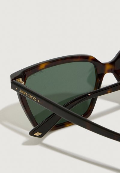 Tortoiseshell slnečné okuliare so zelenými šošovkami, ostré línie, zlaté logo "JIMMY CHOO" na spánku a štýlové čierne akcenty.