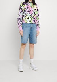 Felpa con cappuccio colorata e motivo, con dettagli rosa, abbinata a pantaloni bermuda in denim. Indossata con sneakers bianche e calzini al ginocchio.
