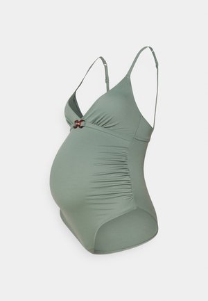 Maillot de bain de maternité en vert doux, fabriqué en tissu extensible. Présente des fronces sur les côtés et un matériel décoratif rouge au centre.