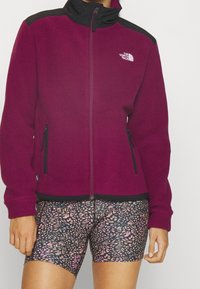 Fleecejacka i mörk magenta med svarta detaljer, full dragkedja och två sidofickor. Matchad med mönstrade tajta shorts i rosa och svart.