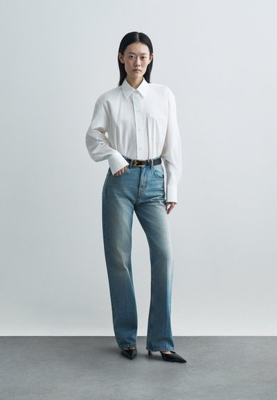 Λευκό πουκάμισο με κουμπιά και τσέπη στο στήθος, σε συνδυασμό με ανοιχτό μπλε τζιν, που διαθέτει ευθεία γραμμή και ελαφριά φθορά. Μαύρες μυτερές γόβες.