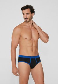 Schwarze Unterwäsche mit blauen Akzenten, ausgestattet mit einem kontrastierenden Bund und Nahtdetails, aus einem weichen, dehnbaren Stoff für mehr Komfort.