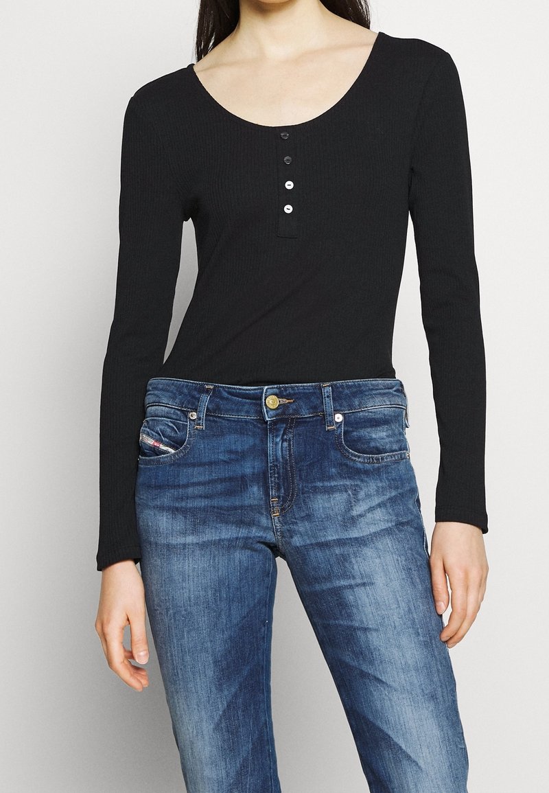 Svart ribbad långärmad topp med en rundad halsringning och fyra knappar, i kombination med blåjeans i denim med subtila blekningar.