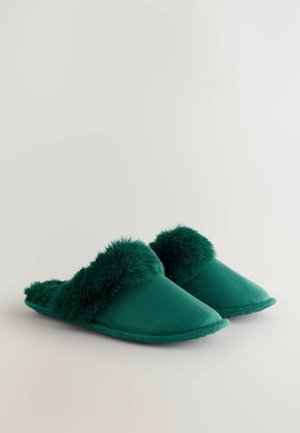 Zöld papucs sima szövet felsőrésszel és plüss, bolyhos szőrrel díszítve. Slip-on dizájn és hegyes orrú forma jellemzi.