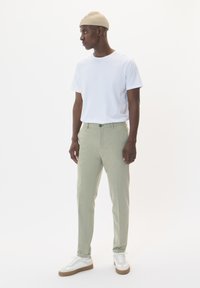 Light green trousers with a tailored fit, paired with a white T-shirt and a beige knitted beanie. Sneakers feature white and tan accents.
