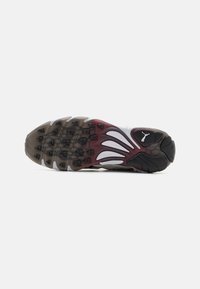 Semelle de chaussure de sport avec un design de semelle à motifs multiples, principalement noire et grise, avec des accents bordeaux et une texture en caoutchouc lisse.