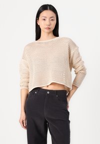 Beige knitted cropped sweater with a loose fit, featuring a textured pattern and long sleeves, paired with high-waisted black pants.