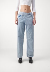 Jeans de tiro alto de color azul claro, de pierna ancha y confeccionados en material de denim con un ajuste relajado. Presenta una costura diagonal única y bolsillos laterales. Combinados con botas de tobillo negras.