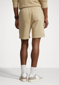 Beige bomullsshorts med elastisk midja, bakficka och uppvikta fållar; i kombination med vita strumpor och ljusgråa avslappnade sneakers.