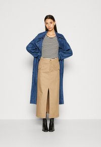 Denim trenčkot, pruhovaný čierno-biely top, béžová midi sukňa s predným rozparkom a čierne členkové čižmy. Kabát má veľké klopy a voľný strih.