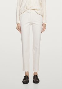 Witte, op maat gemaakte broek met een smalle pasvorm, gladde textuur, zonder zichtbare zakken, gecombineerd met zwarte loafers met een franjerand.