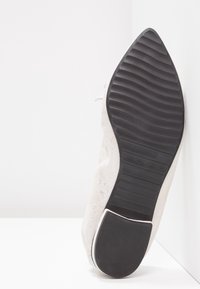 Scarpa in suede con punta affusolata, caratterizzata da una suola in gomma nera testurizzata, una tomaia beige chiaro e dettagli in pizzo minimalista.