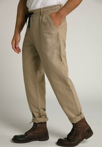 Pantalons en coton beige avec une taille élastique et un cordon de serrage bleu marine, avec des poches latérales et des poignets retroussés, associés à des bottes à lacets marron.
