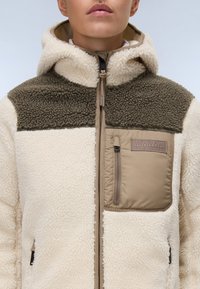 Chaqueta de forro polar en crema y verde oliva, con un bolsillo en el pecho con cremallera, capucha y tejido texturizado con un panel liso de acento.