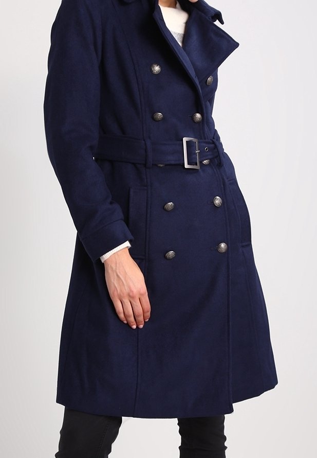 Mörkblå dubbelknäppt kappa med bälte i midjan, silverfärgade knappar och slagkrage. Materialet verkar mjukt och texturerat.
