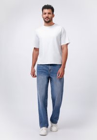 Camiseta blanca de manga corta combinada con jeans rectos de color azul claro y zapatillas blancas, sobre un fondo plano.