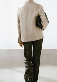 Blazer beige clair à coupe ajustée, associé à un pantalon ample foncé. Le blazer présente des épaules structurées et des boutons décoratifs.