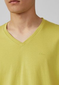 T-shirt en coton jaune à col V, mettant en avant un logo s.Oliver discret brodé dans un fil assorti, texture légère et coupe classique.