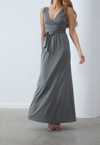 Pitkä, kääntötyylinen mekko pehmeästä harmaasta kankaasta, syvällä V-pääntiellä, istuvalla vyötäröllä ja solmittavalla vyöllä. Sileä pinta ja virtaava siluetti.
