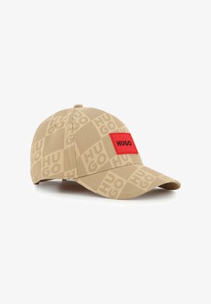 Casquette beige avec un motif répétitif de logos, une forme structurée, et un patch rectangulaire rouge avec l'inscription "HUGO" en lettres noires.