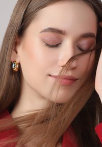 Goldene Creolen mit einem blauen Edelsteinakzent, getragen von einer Person mit langen, glatten Haaren, die einen ebenmäßigen Hautton und dezentes Makeup hat.