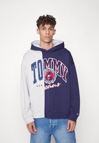 Grå og marineblå hettegenser med delt design som har stort "TOMMY"-logo og grafikk. Blandingsmateriale av bomull; ribbede mansjetter; avslappet passform.